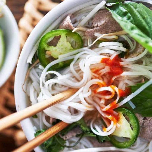 A close-up picture of a bowl of Vietnamese pho noodle soup topped with beef, basil, jalapeño, and cilantro.