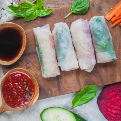 Four spring rolls on a cutting board. The rolls contain rice noodles, shrimp, lettuce, and basil.